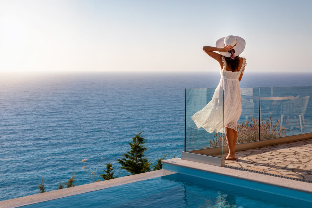 A woman in a white dress stands beside the pool, admiring the ocean view, symbolizing boutique in hotel affiliate marketing.