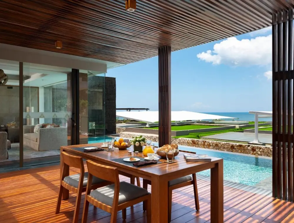 Anantara Uluwatu, a Bali resort all inclusive, features a dining table and chairs on the deck, offering stunning ocean views