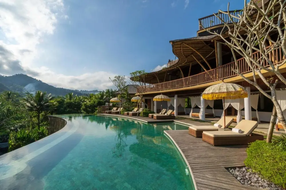 The pool at Wapa di Ume Sidemen, a beach resort in Bali, situated among tall trees, offers a peaceful escape for guests to relax.