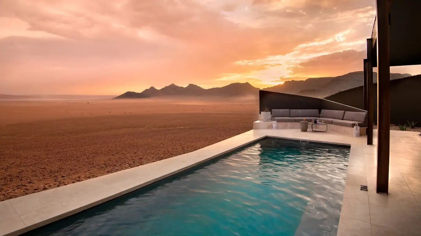 The pool at &Beyond Sossusvlei Desert Lodge glows under a sunset, showcasing why it's one of the best desert hotels worldwide.