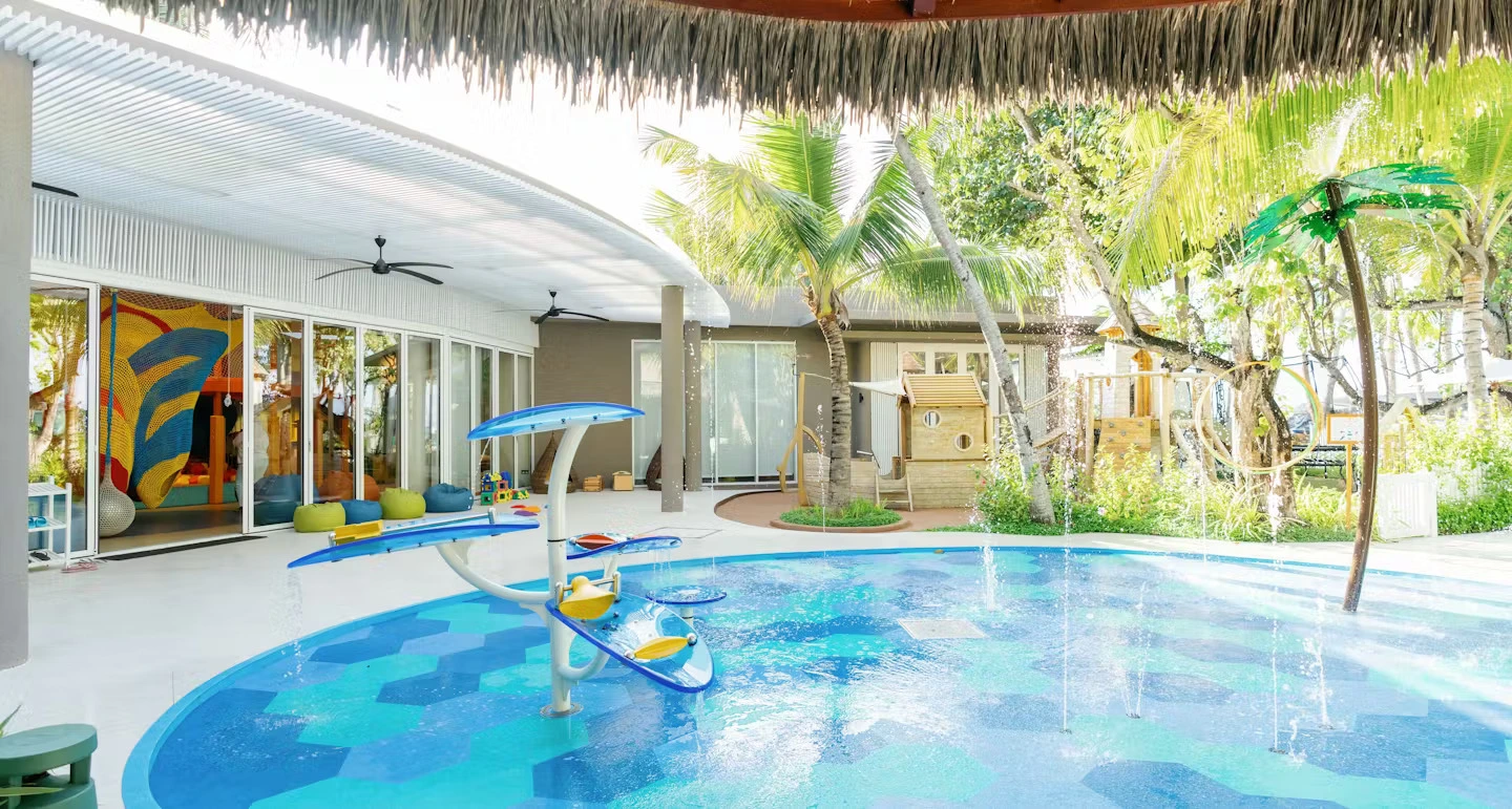 A vibrant pool featuring a water slide, surrounded by a sandy beach area at Cheval Blanc Randheli, a family hotel in Maldives.