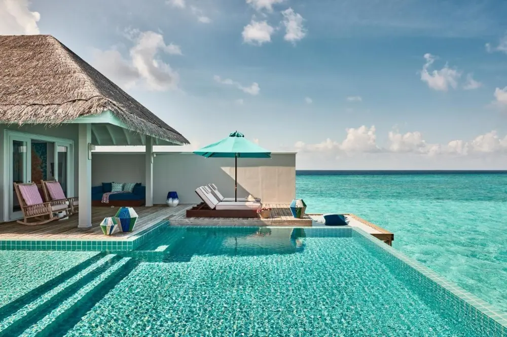 A beautiful pool area with lounge chairs and a thatched roof, designed for family enjoyment at Finolhu, a leading family hotel in Maldives.