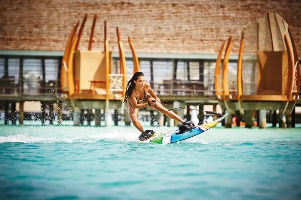 A woman wakeboards in the ocean, showcasing her skills near the luxurious Lux* South Ari Atoll, family hotel in Maldives.