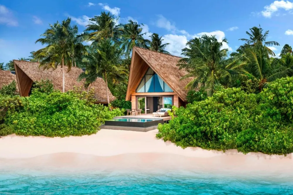 A stunning tropical beach scene with palm trees and thatched huts, set at The St. Regis Vommuli Resort, one of the best family hotels in Maldives.