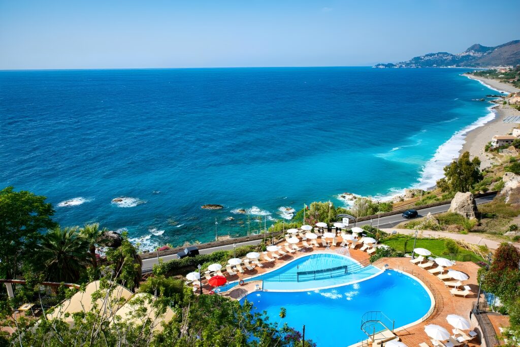 Beautiful scene of the pool and beach at Hotel Baia Taormina, representing the allure of this hotel in Sicily with private beach.