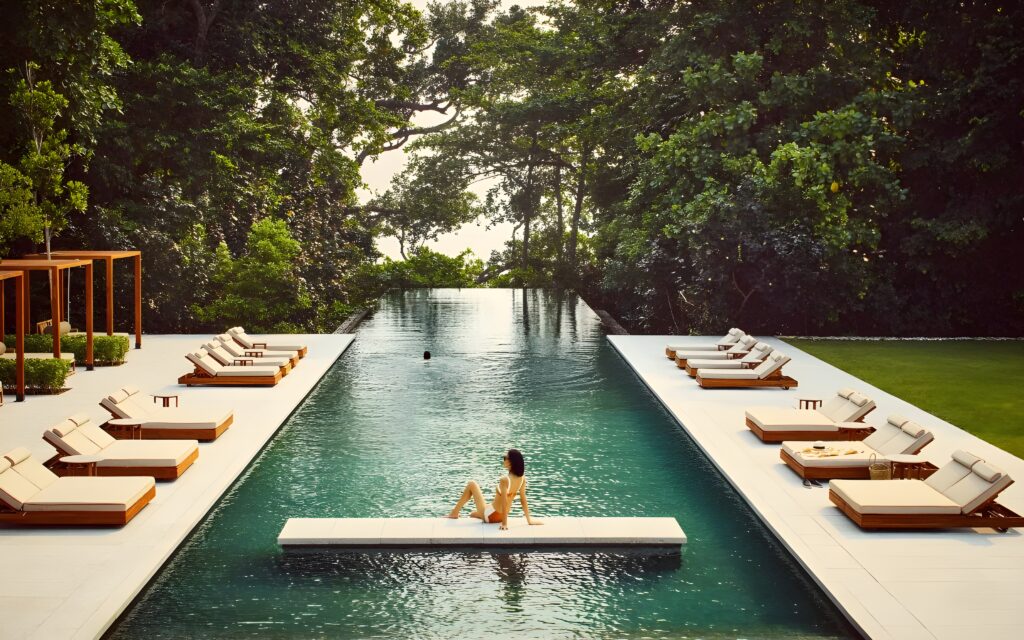 A woman relaxes on a lounge chair by the pool at One&Only Desaru Coast, Malaysia, enjoying a serene moment in luxury.