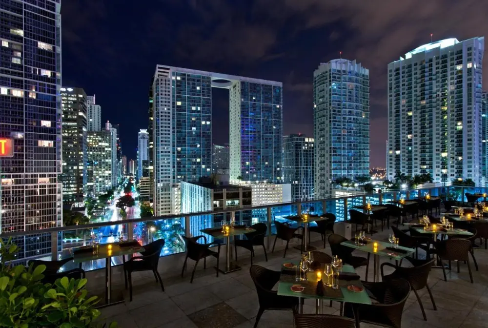 A rooftop bar at Kimpton EPIC Hotel, one of the best party hotels in Miami, features lounge chairs and umbrellas, offering views of the city.