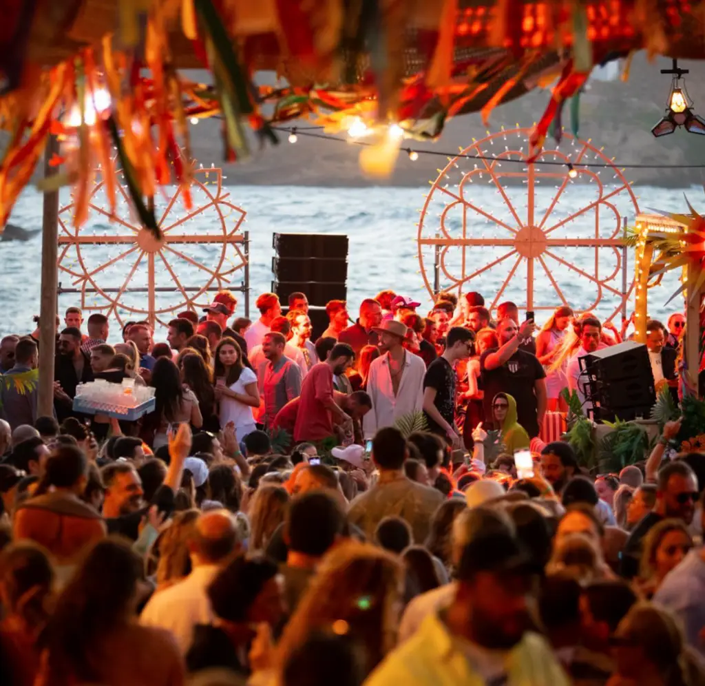 A lively beach party with a crowd enjoying the sun, featuring Boheme Mykonos, one of the best hotels in Mykonos for party fun.