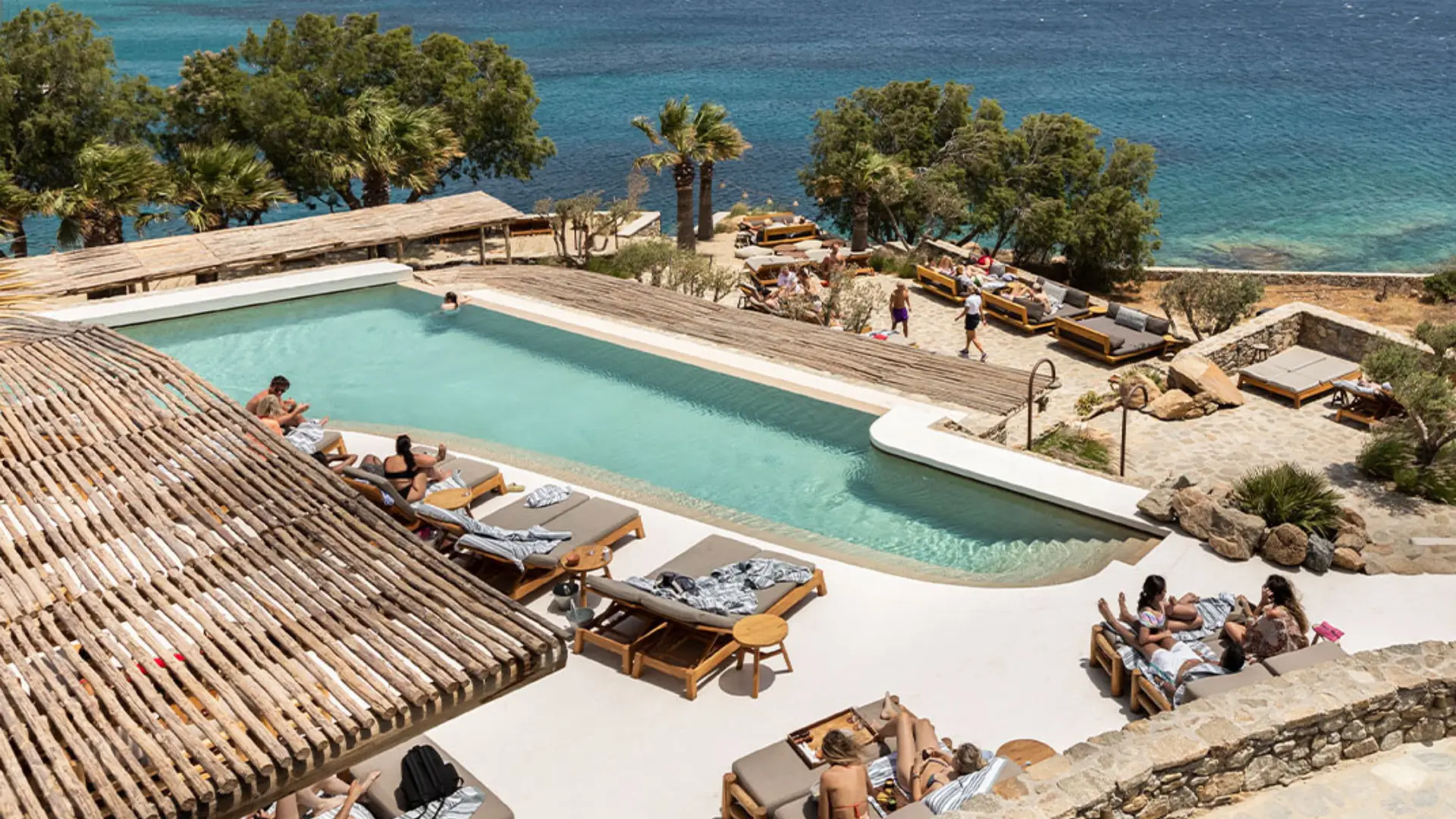 A vibrant pool at Soho Roc House, surrounded by palm trees, perfect for fun at one of the best hotels in Mykonos for party lovers.