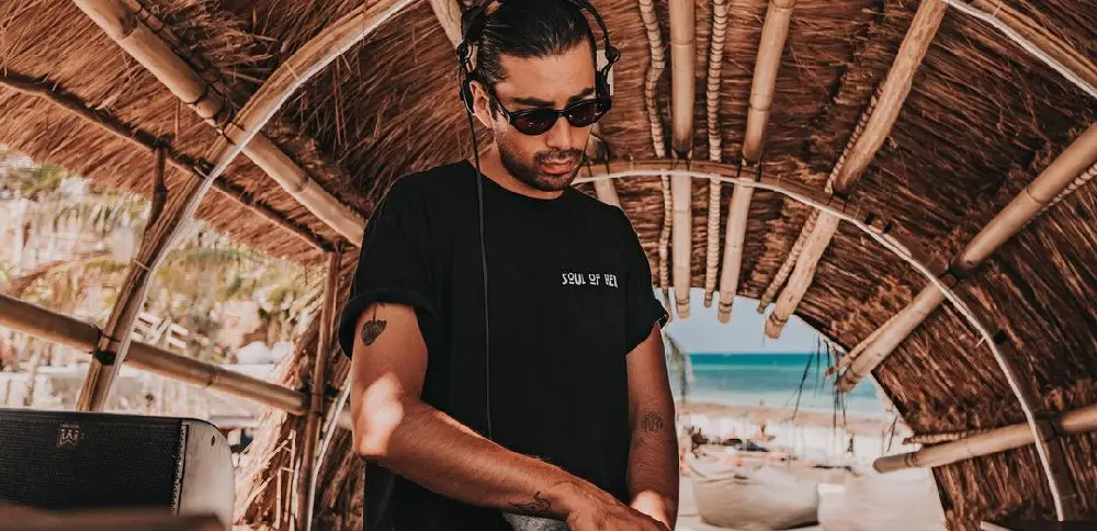 A man wearing sunglasses plays music on the beach, capturing the fun at the best party hotels in Tulum, like Papaya Playa Project.