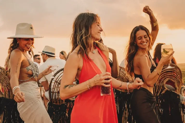 At the beach, three women in red dresses and hats dance happily, showcasing the vibe of the best party hotels in Tulum.