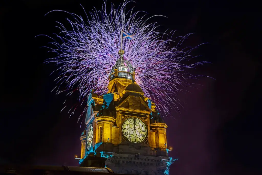 Purple fireworks illuminate the sky as the clock strikes midnight at The Balmoral, one of the best hotels to celebrate New Year's Eve in Edinburgh.