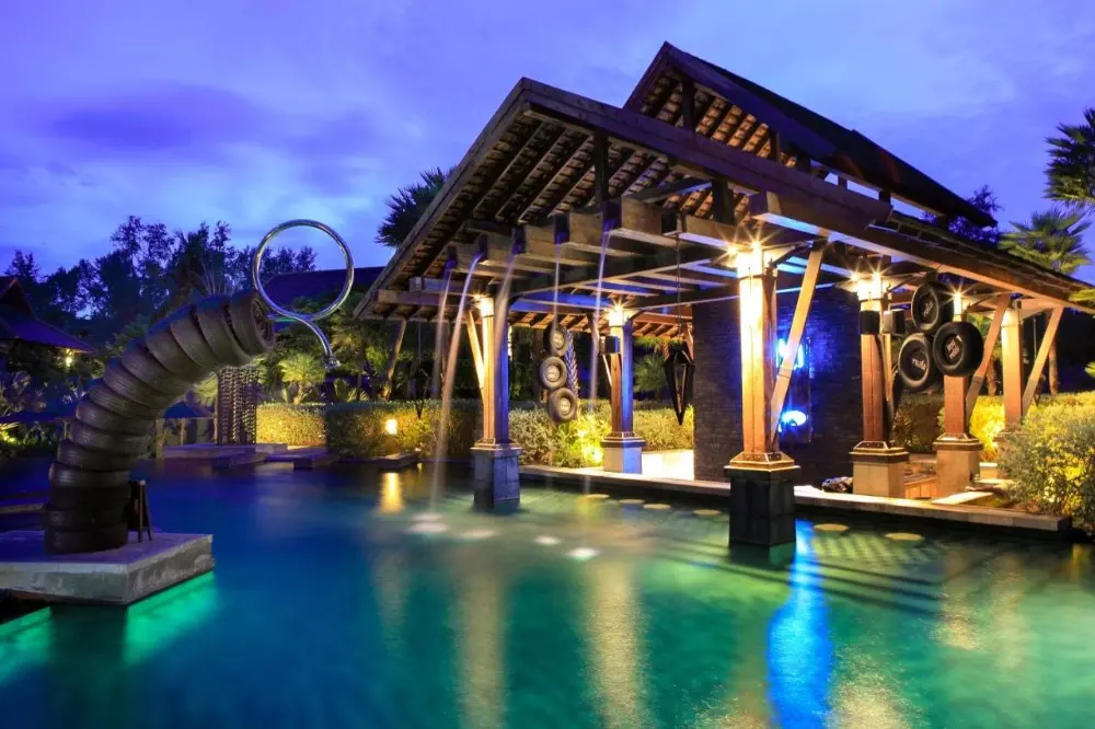 A tranquil night view of a pool with a waterfall and gazebo, showcasing the beauty of The Slate resort in Phuket, Thailand.