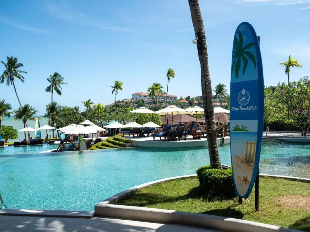 A large pool at Pullman, one of the best resorts in Phuket for couples, featuring a surfboard and umbrellas.