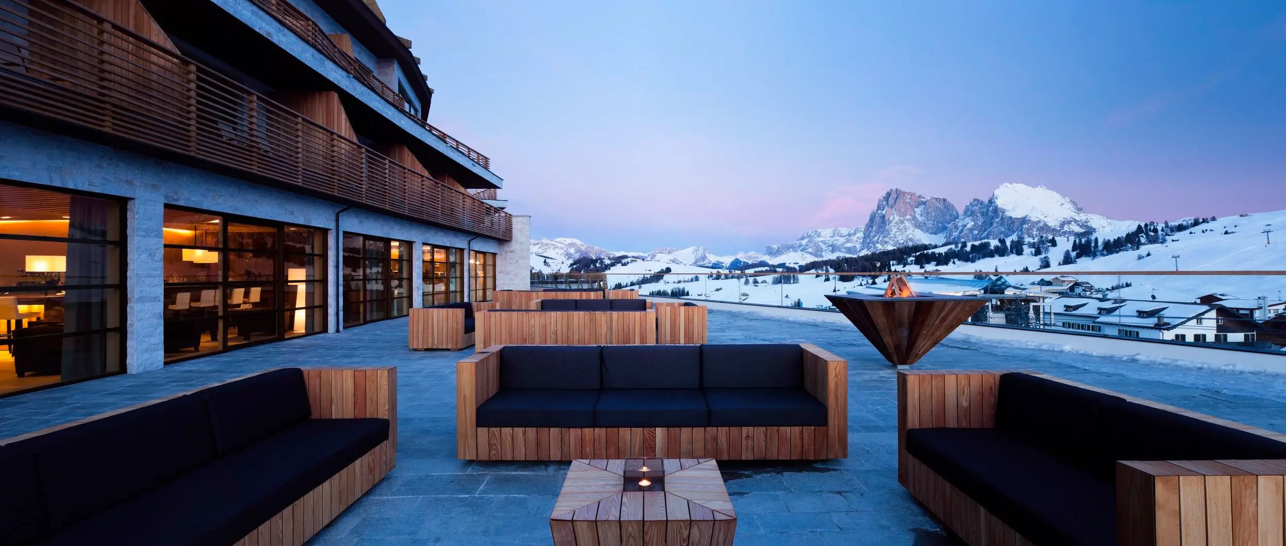 Cozy patio at Alpina Dolomites Lodge, one of the best ski hotels in Italy, with couches and tables, offering stunning mountain views.