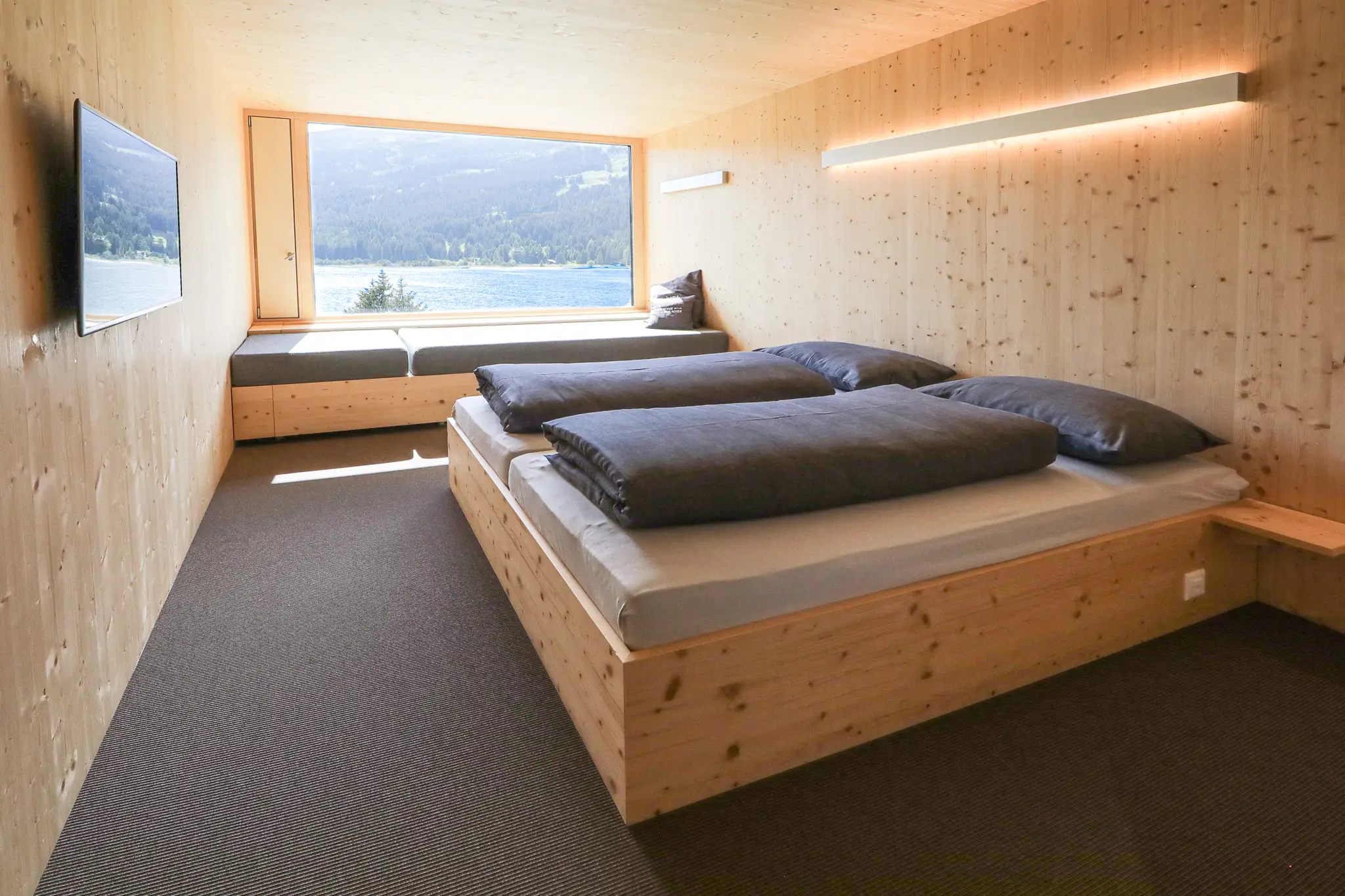 Comfortable bedroom with a bed and a TV on the wall, a great spot to relax at Rivier Mountain Lodge Lenzerheide, one of the best snowboarding hotels in Switzerland.