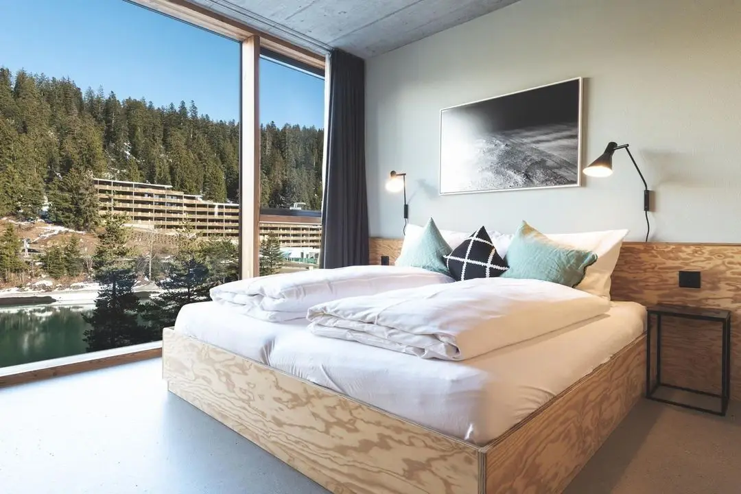 Cozy bedroom at Riders Hotel Laax, one of the best snowboarding hotels in Switzerland, featuring stunning mountain and lake views.