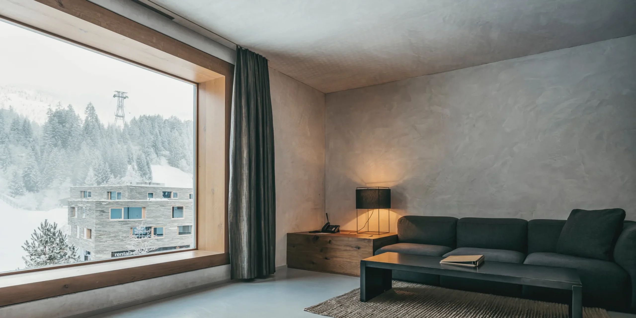 Bright room at Rock Resort Laax with a comfy couch and a window view of the mountains, a top choice among the best snowboard hotels in Switzerland.