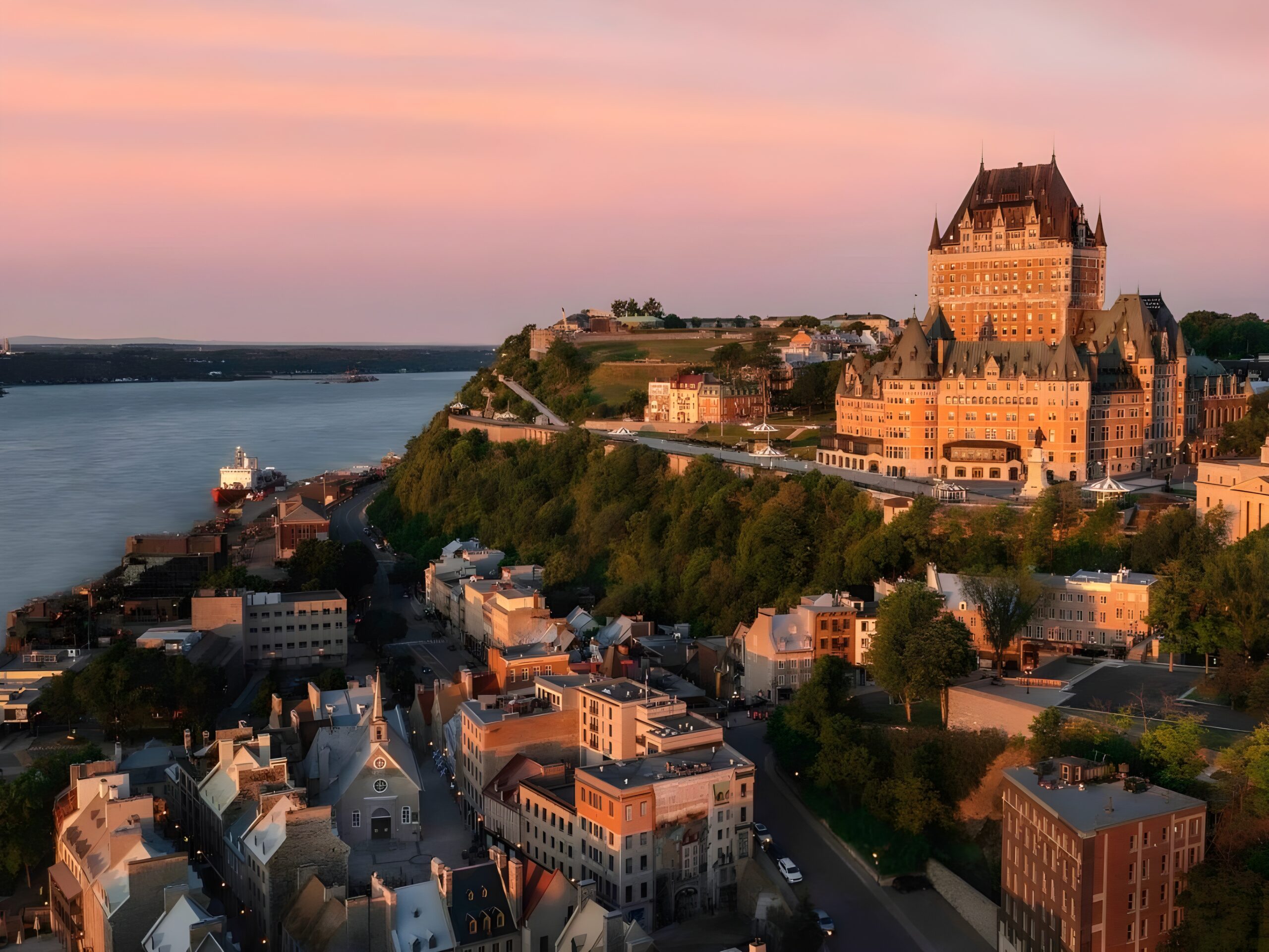 View of Quebec City from a hill, showcasing Fairmont Le Château Frontenac, one of the best castle hotels in the world, beside the beautiful water.