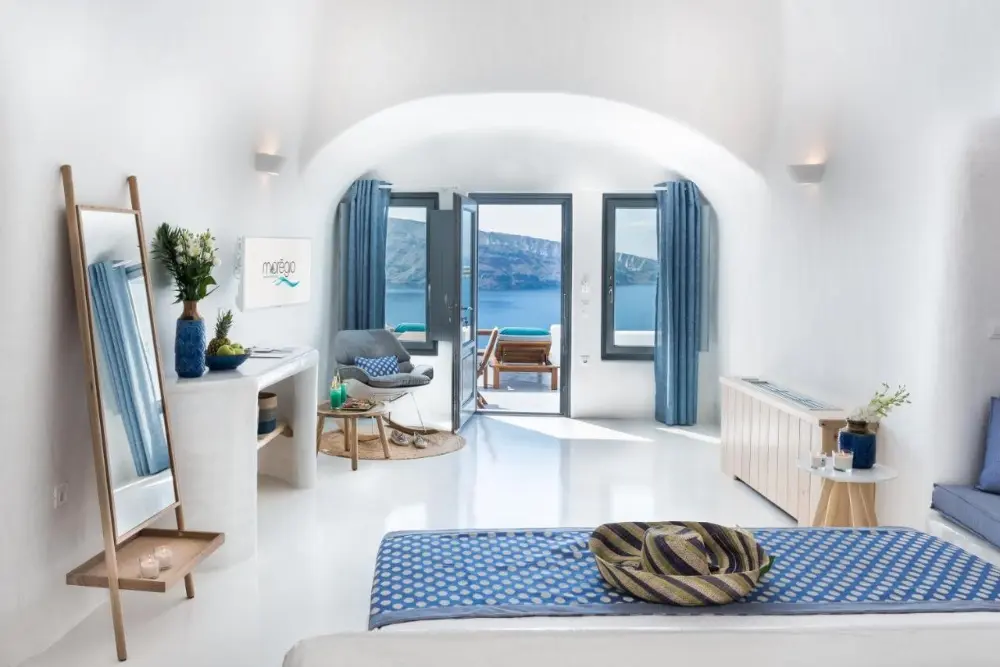 A beautiful bedroom at Maregio Suites, a design hotel in Santorini, featuring a blue bed and a stunning ocean view.