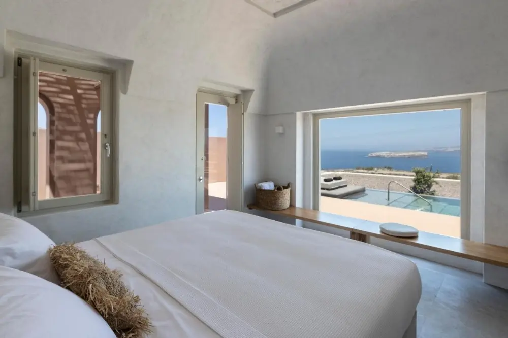 Enjoy a peaceful bedroom at Serra Exclusive Suites, complete with a bed and a beautiful view of the ocean, a top choice for a design hotel in Santorini.