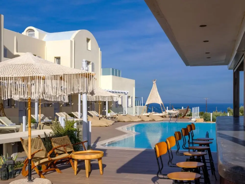 A peaceful pool area with lounge chairs and umbrellas, offering a stunning ocean view at Aliter Suites, a family-friendly hotel in Santorini.