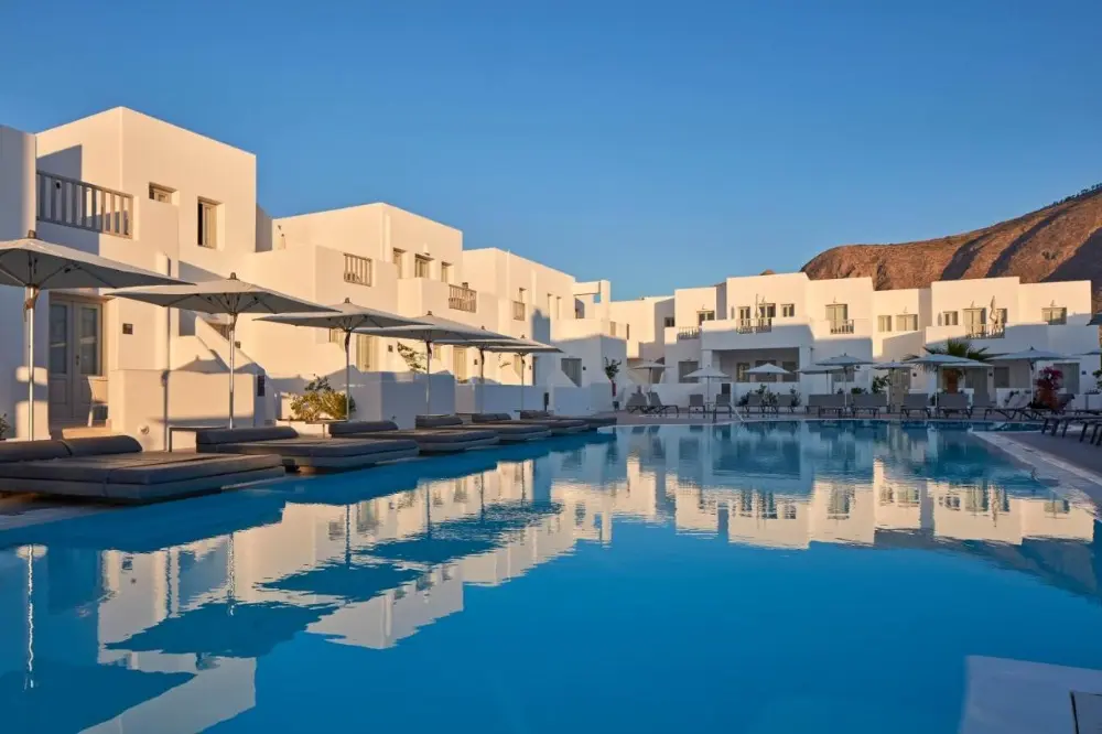 A tranquil pool at Aqua Blue Hotel, surrounded by elegant white structures, ideal as a family-friendly hotel in Santorini.