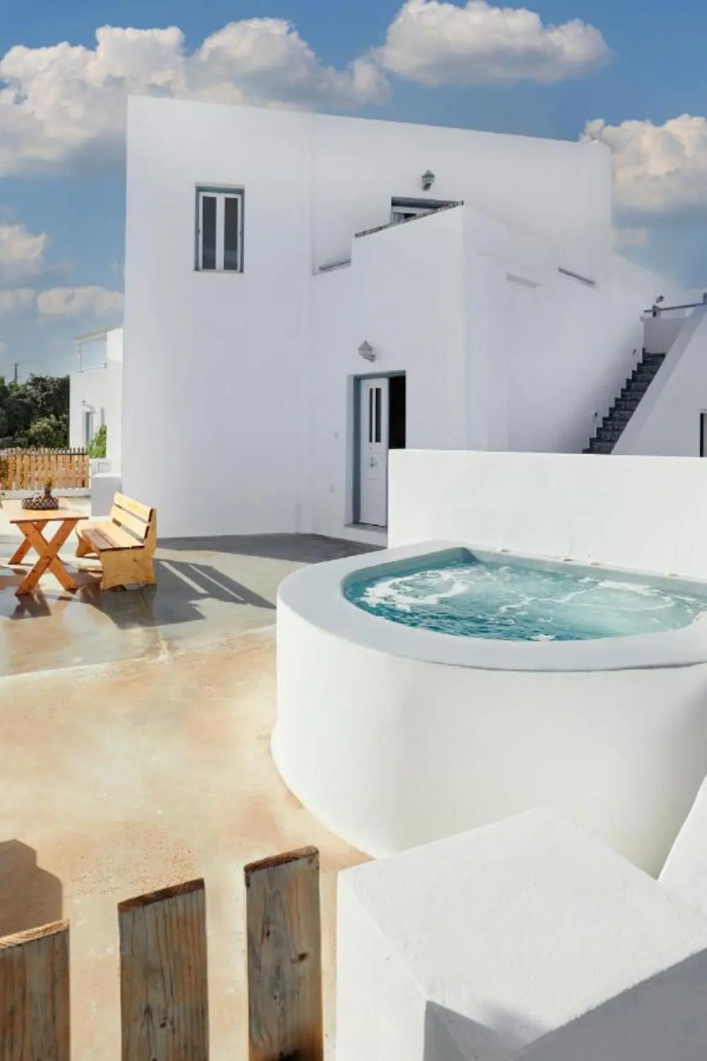 The outside of a white suite equipped with a hot tub and wooden furniture, located the family-friendly hotel Athiri Santorini.