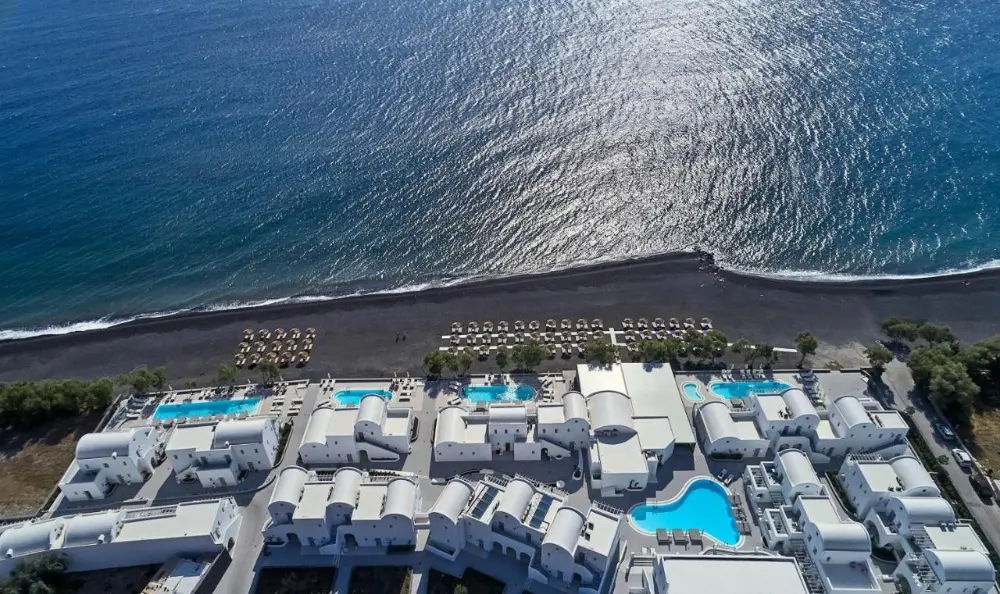 Aerial image of the beach and Costa Grand Resort & Spa, emphasizing itself as a family-friendly hotel in Santorini.