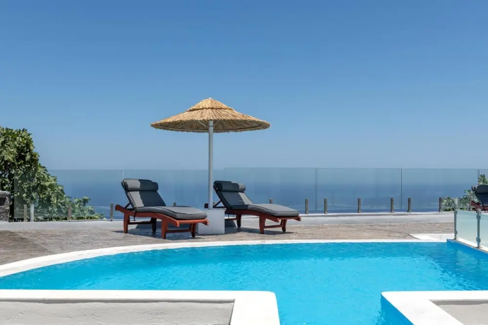 The pool area at Splendour Resort, family-friendly hotel in Santorini featuring lounge chairs and umbrellas with a stunning Aegean sea view.