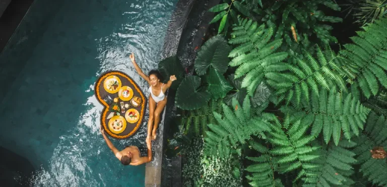 An influencer couple enjoys a meal in a pool, surrounded by lush green plants, showcasing hotel marketing on Instagram.