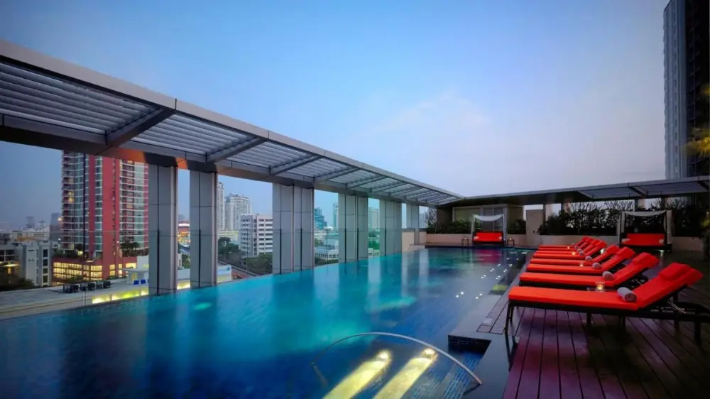 Large swimming pool surrounded by red lounge chairs at Marriott Sukhumvit, a luxury hotel in Bangkok, Thailand, featuring a stunning city view.