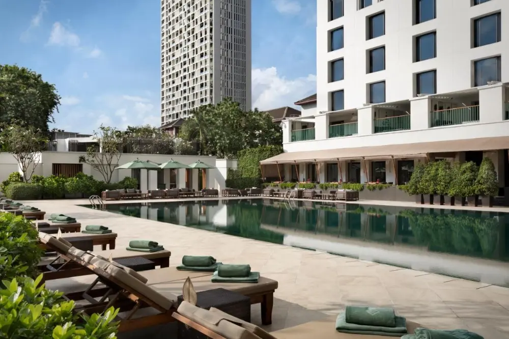 The pool at Sukhothai, a luxury hotel in Bangkok, Thailand, is surrounded by lounge chairs, offering the perfect relaxing spot.