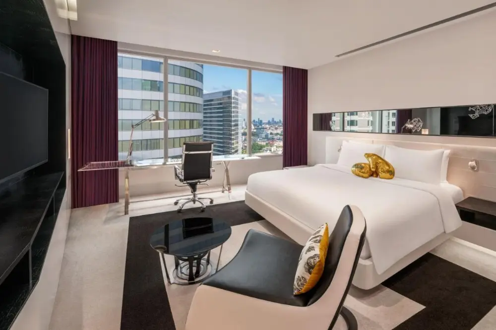 A hotel room at W Bangkok, a luxury hotel in Bangkok, Thailand, featuring a large bed, television, and stunning city view.