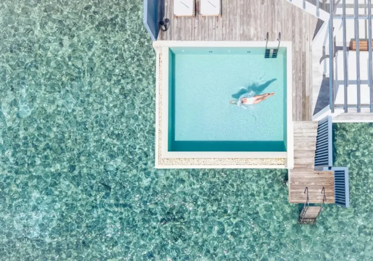 A breathtaking aerial view of a luxury resort in the Maldives, featuring a stunning pool surrounded by the vast ocean, capturing the essence of the island's beauty.