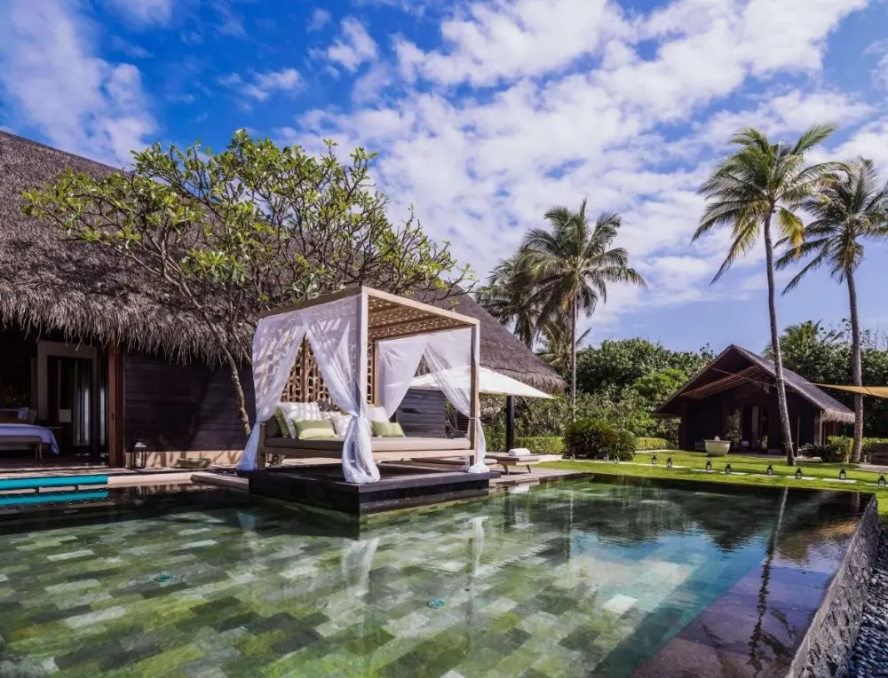 The resort's pool at One & Only Reethi Rah, a luxury resort in Maldives Island, is beautifully surrounded by palm trees, highlighting the Maldives' luxury experience.