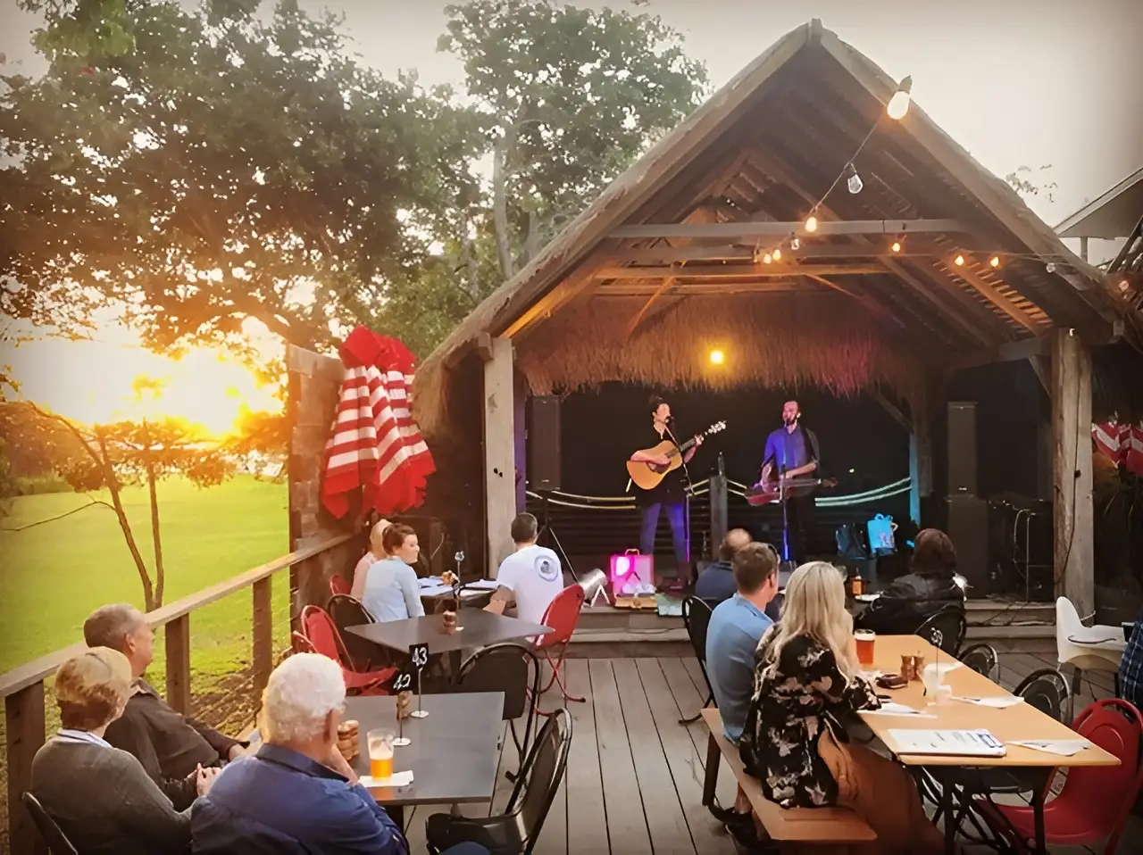 Two people singing and playing a guitar on a small cosy stage in front of a few people at Boogie Woogie Beach House, one of the best music-themed hotels worldwide.