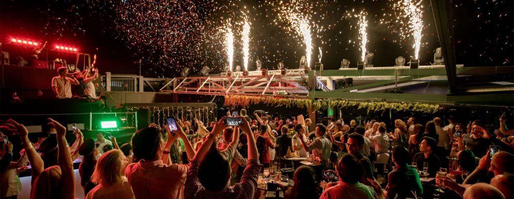 Guests celebrate at a vibrant party in Bangkok's SO Hotel, surrounded by DJ equipment and lively atmosphere.