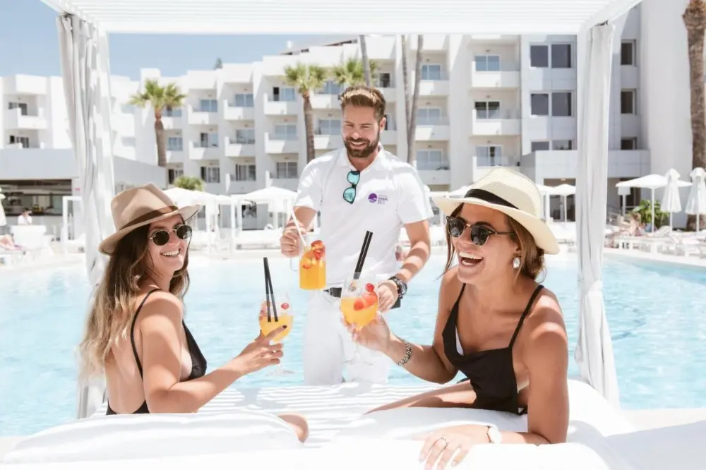 Three women relax on a lounge chair at Hotel Garbi Ibiza & Spa, enjoying drinks in a vibrant party hotel in Ibiza atmosphere.