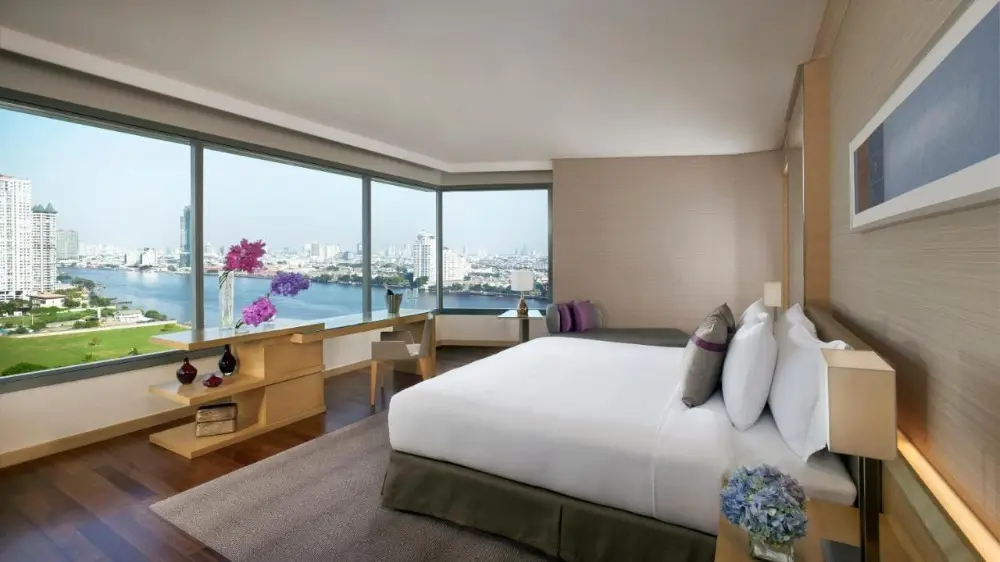 A romantic hotel in Bangkok, Avani Plus Riverside, features a cozy room with a stunning view of the river and city skyline.