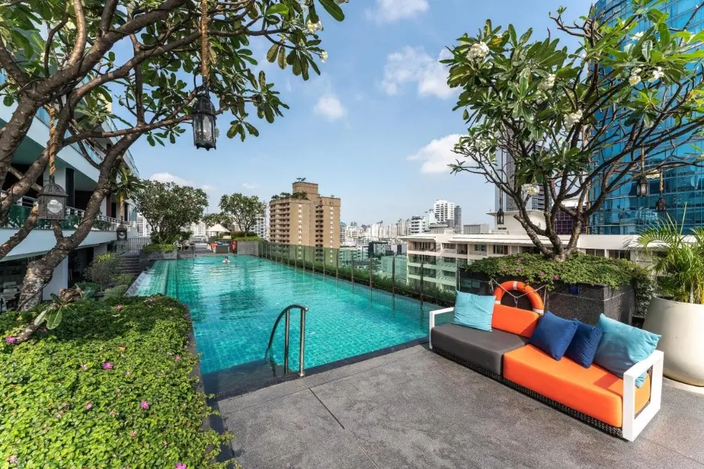 The pool at Muu, a romantic hotel in Bangkok, is beautifully surrounded by lush trees and vibrant plants.