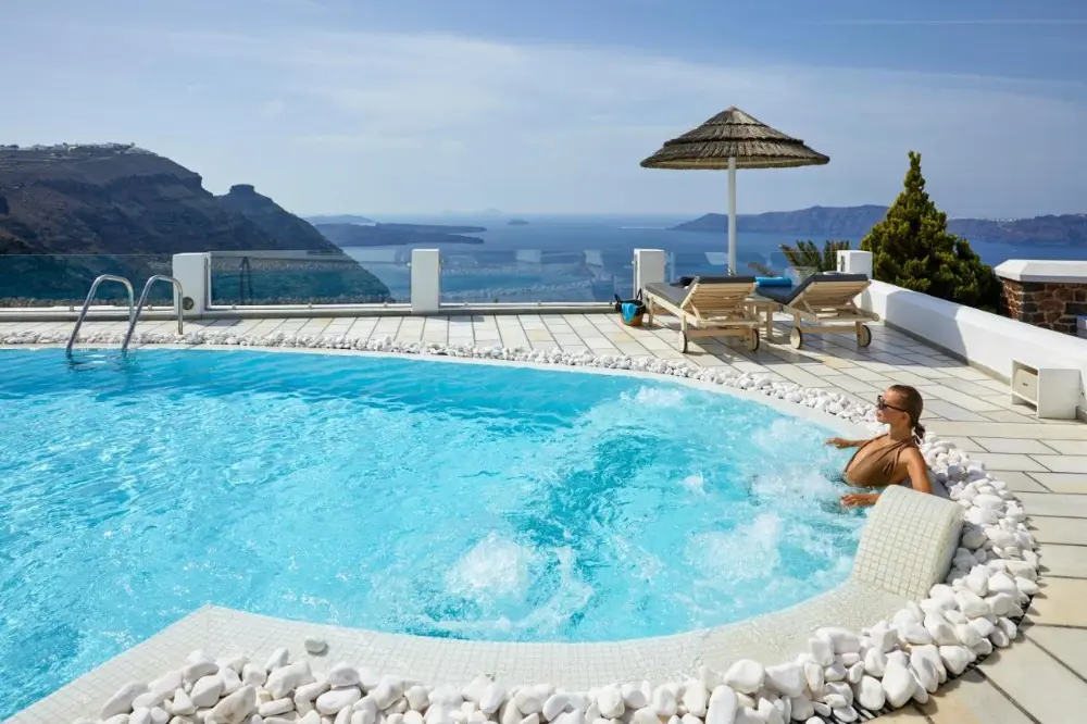 A woman enjoys the sun while relaxing in a pool at a spa hotel in Santorini.