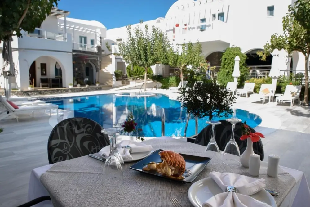 A dinner table elegantly arranged by a swimming pool at La Mer Deluxe, a spa hotel in Santorini.