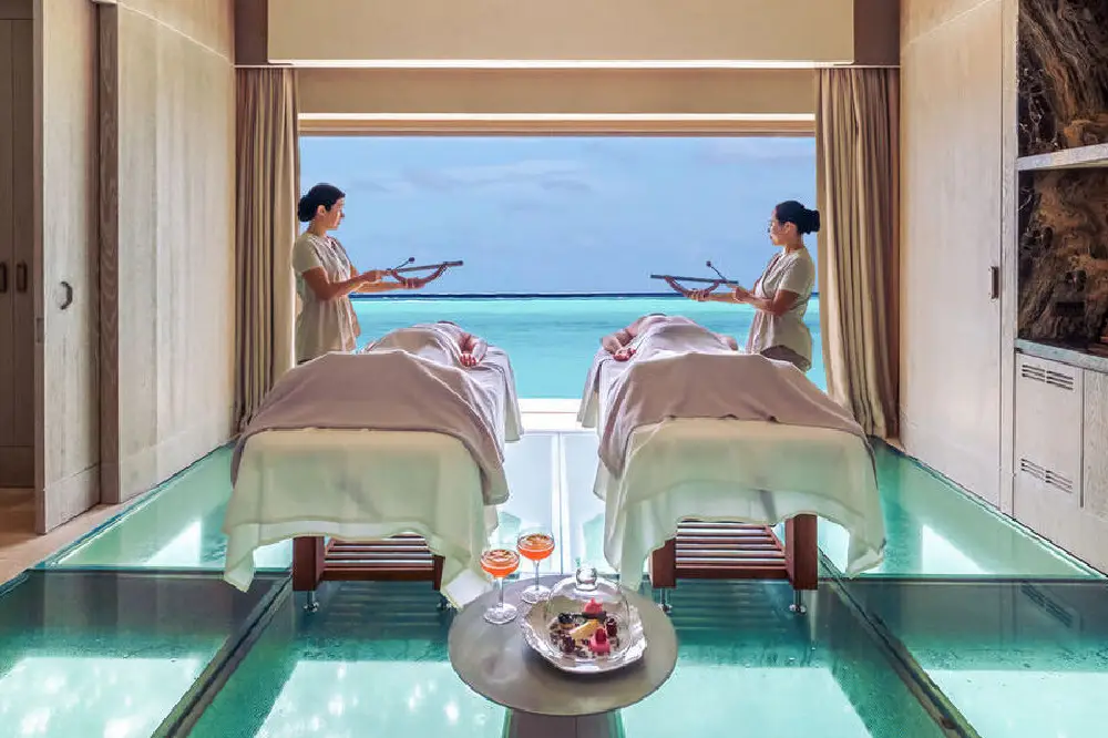 In a spa room at Joali Being, spa resort in Maldives, two people indulge in relaxation while overlooking the beautiful ocean.