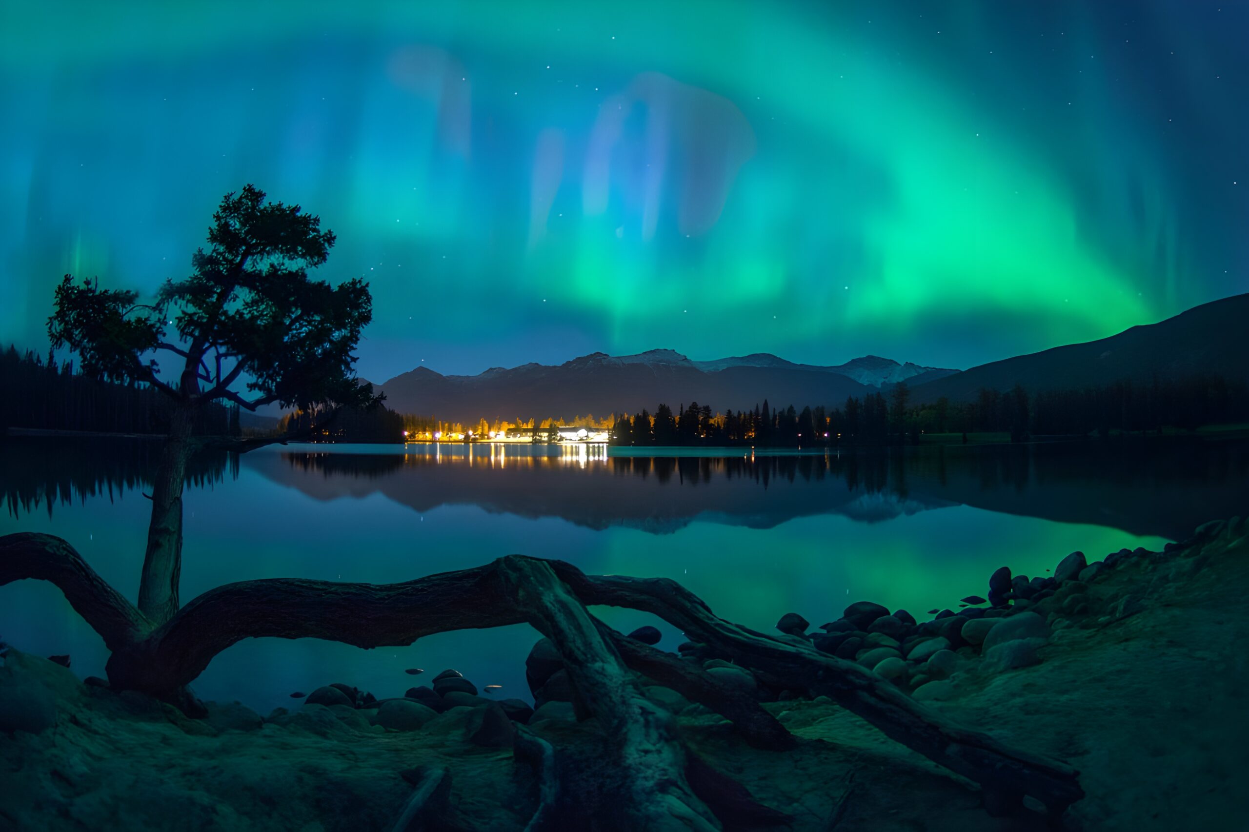 A breathtaking display of the aurora borealis dances over a serene mountain lake, viewed from Fairmont Jasper Park Lodge in Canada, a stargazing hotel.