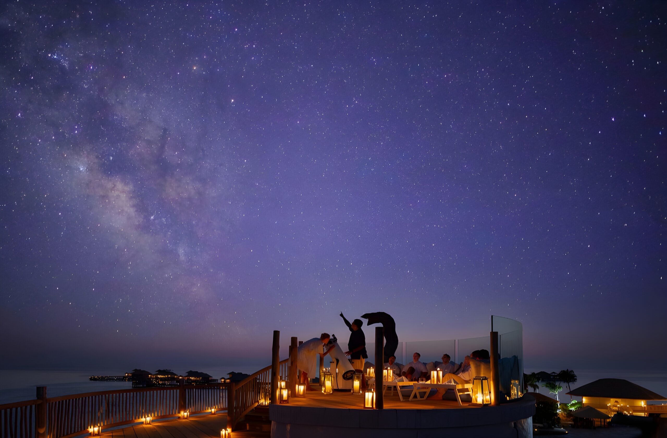 Individuals stand on a deck, admiring the ocean and the Milky Way above, at Soneva Jani, a stargazing hotel in the Maldives.