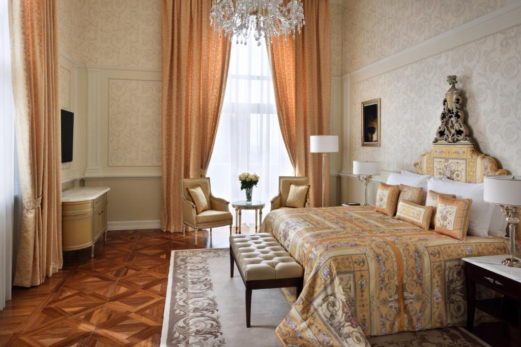 A luxurious bedroom at Palazzo Versace Dubai, design hotel in Dubai, featuring a bed, elegant chair, and a stunning chandelier overhead.